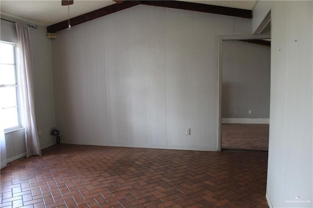 spare room with lofted ceiling with beams, a healthy amount of sunlight, and wooden walls