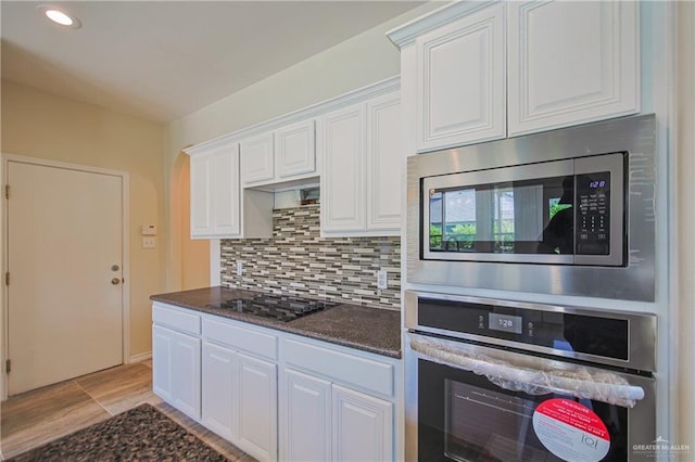 kitchen with white cabinets, appliances with stainless steel finishes, decorative backsplash, and dark stone counters