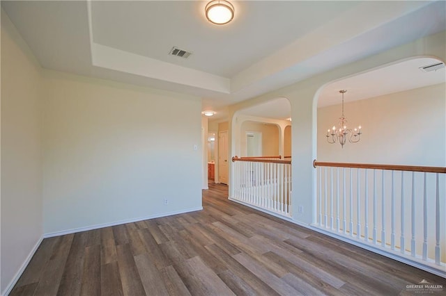 unfurnished room with hardwood / wood-style flooring, a raised ceiling, and an inviting chandelier