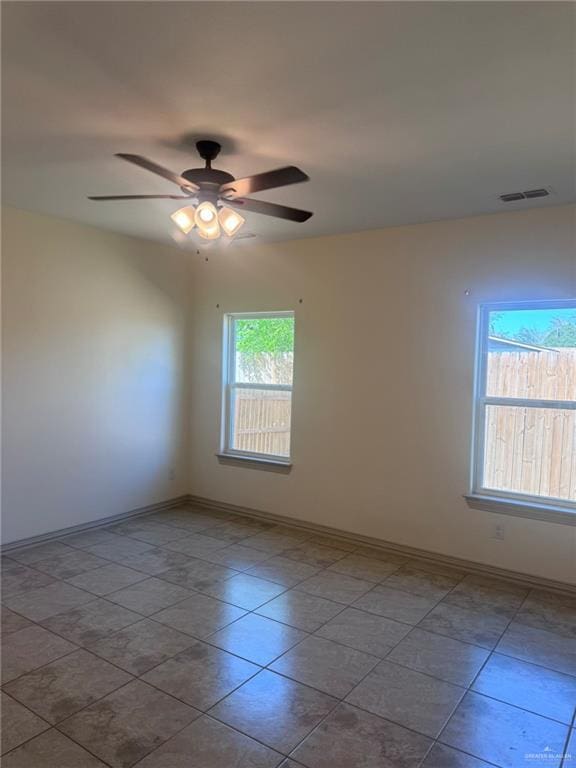 empty room featuring a ceiling fan, visible vents, and baseboards