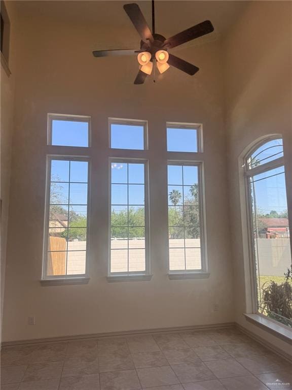 spare room with light tile patterned floors, a high ceiling, a ceiling fan, and baseboards