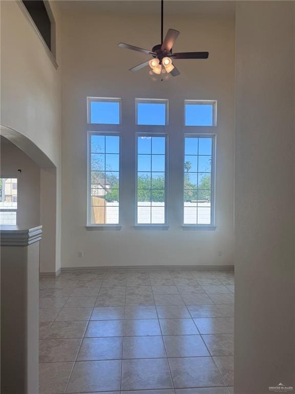 empty room with arched walkways, a high ceiling, light tile patterned flooring, and a healthy amount of sunlight