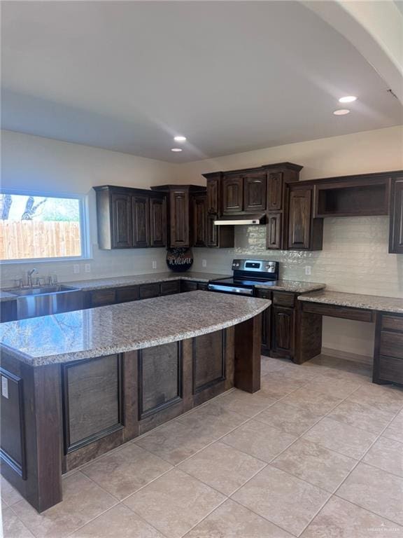 kitchen with light stone counters, backsplash, stainless steel range with electric cooktop, dark brown cabinetry, and under cabinet range hood