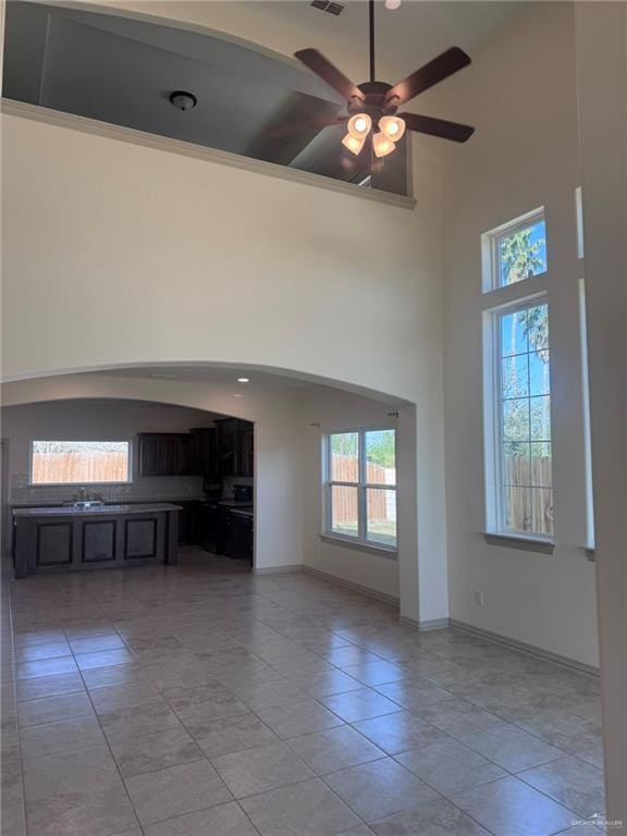 unfurnished living room with arched walkways, light tile patterned floors, a high ceiling, ceiling fan, and baseboards