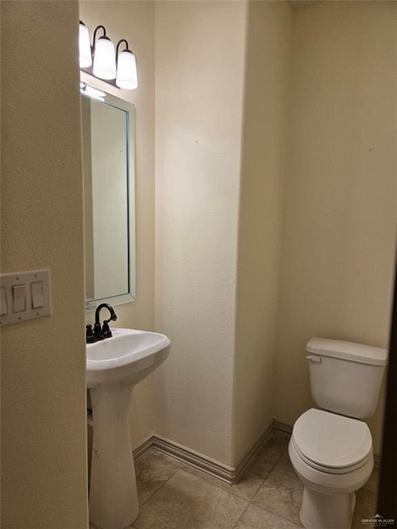 half bathroom with toilet, baseboards, a sink, and tile patterned floors