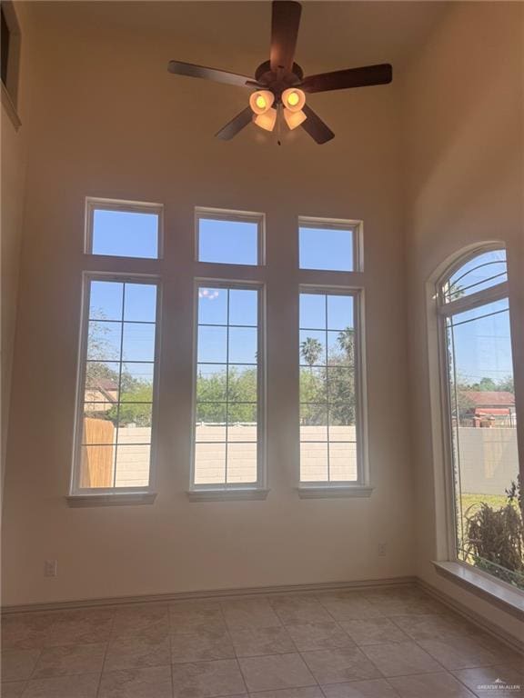 empty room with baseboards, light tile patterned flooring, a towering ceiling, and a healthy amount of sunlight