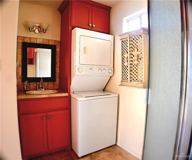 laundry area featuring light tile patterned floors, stacked washer / dryer, and a sink
