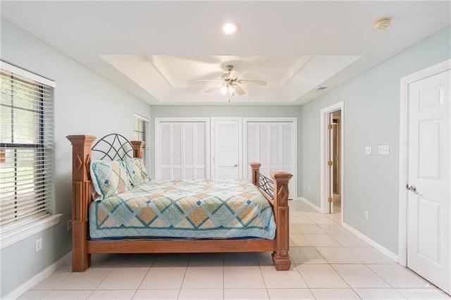 bedroom with light tile patterned floors, a tray ceiling, multiple closets, and ceiling fan