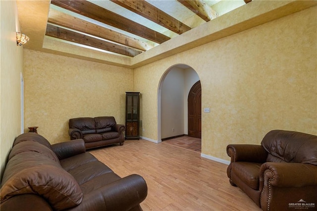 living room featuring a towering ceiling, light hardwood / wood-style flooring, and beamed ceiling