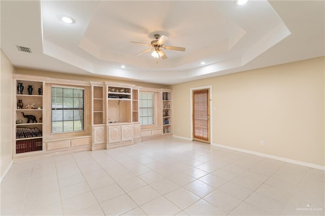 unfurnished living room with built in shelves, a raised ceiling, ceiling fan, and light tile patterned flooring