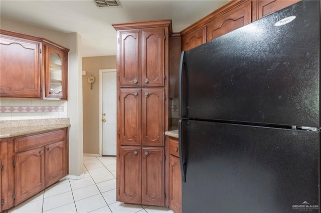 2915 Roselawn Dr, Weslaco, TX 78596 - kitchen featuring freestanding refrigerator, light tile patterned flooring, tasteful backsplash, brown cabinets, and glass insert cabinets