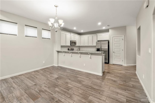 kitchen featuring kitchen peninsula, appliances with stainless steel finishes, a kitchen bar, white cabinets, and light wood-type flooring