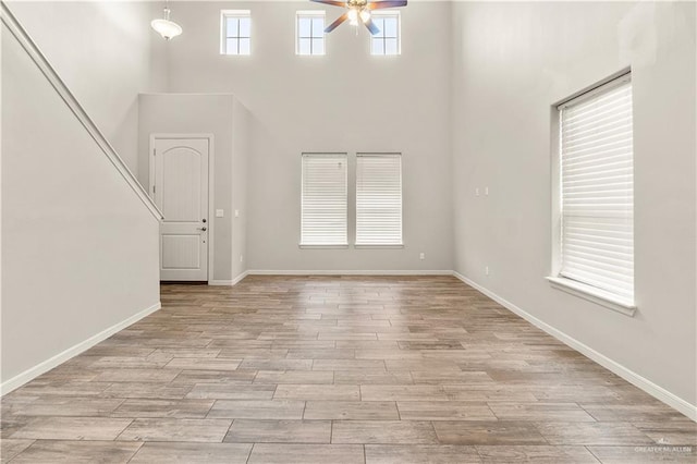 unfurnished living room with a high ceiling, light wood-type flooring, and ceiling fan