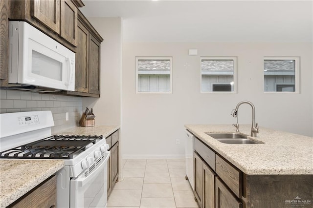 kitchen featuring white appliances, sink, light tile patterned floors, an island with sink, and tasteful backsplash