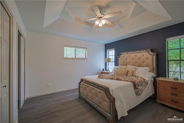 bedroom with ceiling fan, dark wood-type flooring, a tray ceiling, and a closet