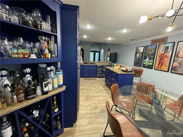 bar with light wood-type flooring, beverage cooler, crown molding, sink, and blue cabinetry