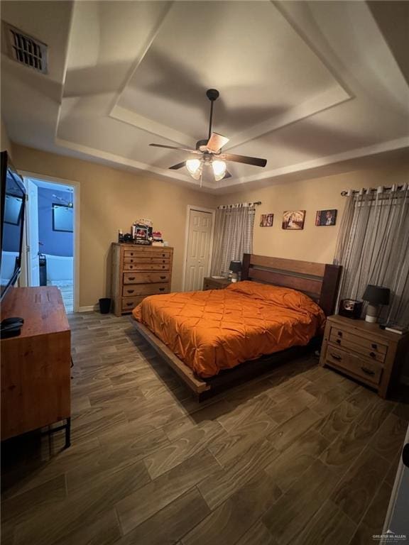 bedroom featuring a tray ceiling, ensuite bath, ceiling fan, and dark hardwood / wood-style flooring