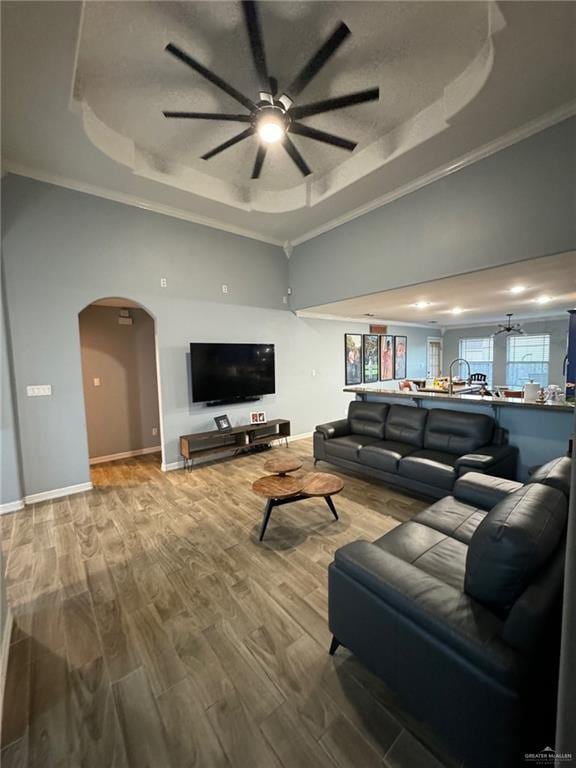 living room with wood-type flooring, a raised ceiling, and ornamental molding