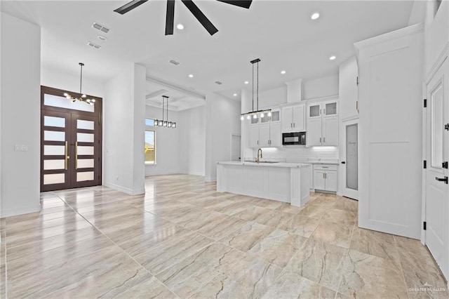 kitchen featuring white cabinets, french doors, decorative light fixtures, and a center island with sink