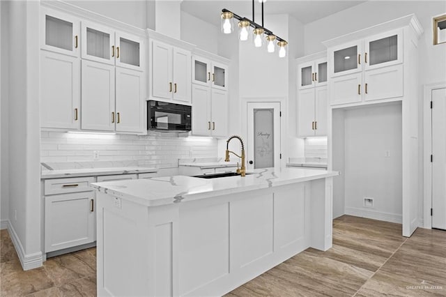 kitchen with sink, hanging light fixtures, light stone counters, a center island with sink, and white cabinets