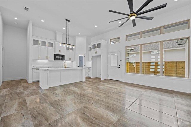 kitchen with backsplash, decorative light fixtures, white cabinetry, and an island with sink