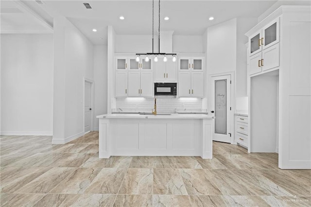 kitchen featuring white cabinets, decorative light fixtures, tasteful backsplash, and a kitchen island with sink