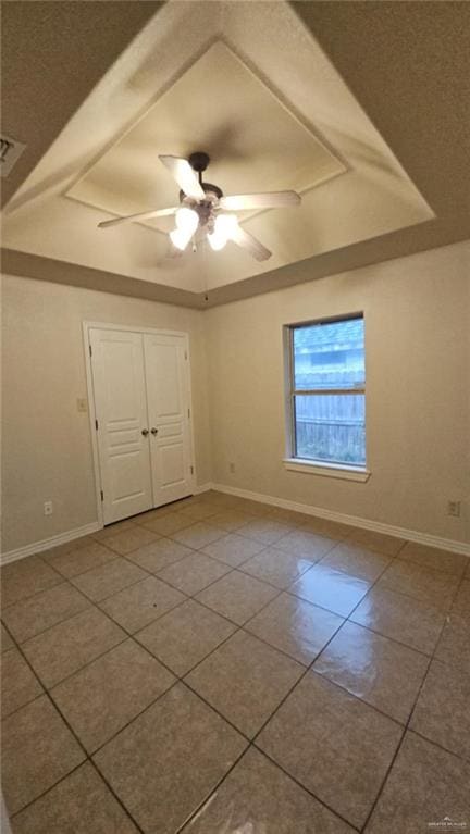 unfurnished room with ceiling fan, a raised ceiling, and tile patterned floors