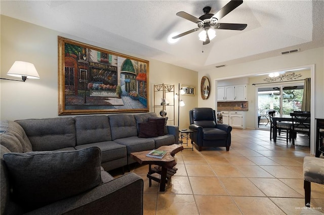 living room featuring ceiling fan, light tile patterned floors, a textured ceiling, and a tray ceiling