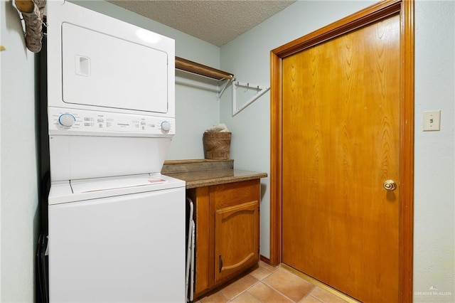 clothes washing area with cabinets, light tile patterned floors, a textured ceiling, and stacked washer and dryer