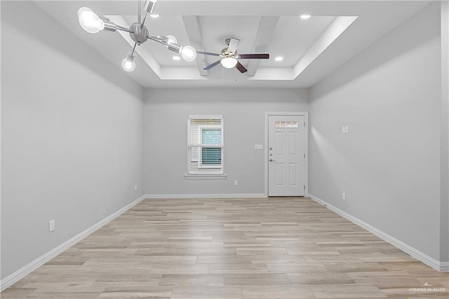 spare room featuring a tray ceiling, ceiling fan, and light wood-type flooring