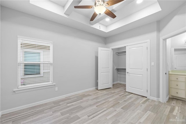 unfurnished bedroom with a closet, ceiling fan, light wood-type flooring, and a tray ceiling