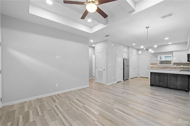 kitchen featuring white cabinetry, light wood-type flooring, stainless steel refrigerator, a raised ceiling, and pendant lighting