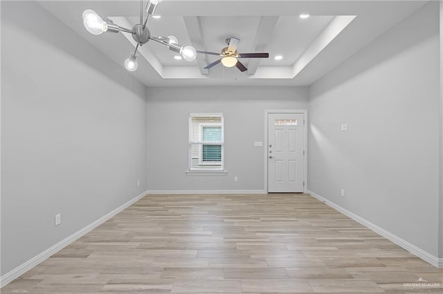 spare room with a raised ceiling, ceiling fan, and light wood-type flooring