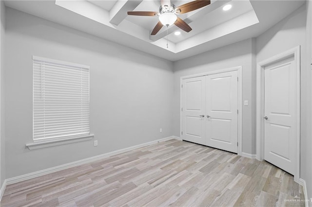 unfurnished bedroom with ceiling fan, a tray ceiling, light wood-type flooring, and a closet