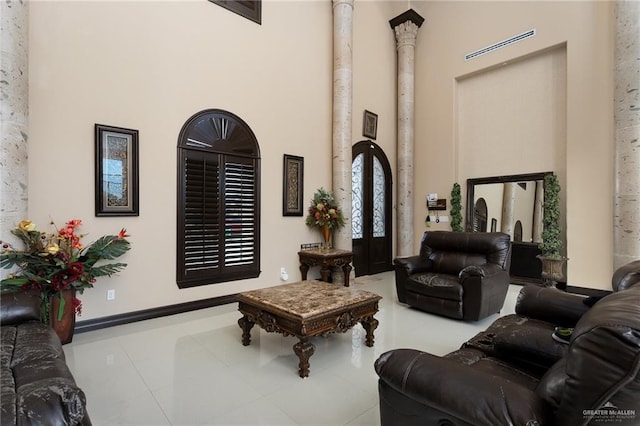 living room featuring decorative columns, a towering ceiling, french doors, and light tile patterned floors