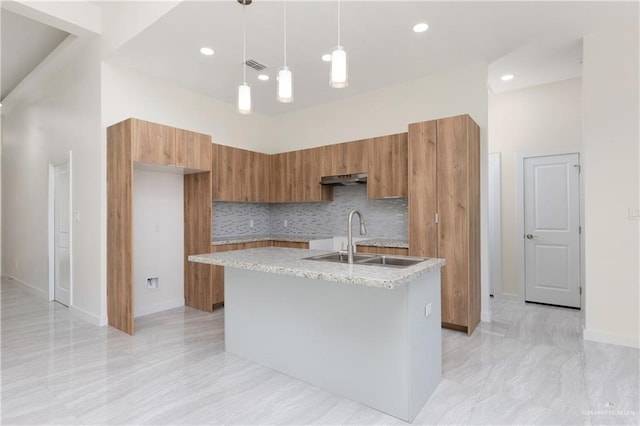 kitchen featuring sink, a high ceiling, an island with sink, decorative backsplash, and decorative light fixtures