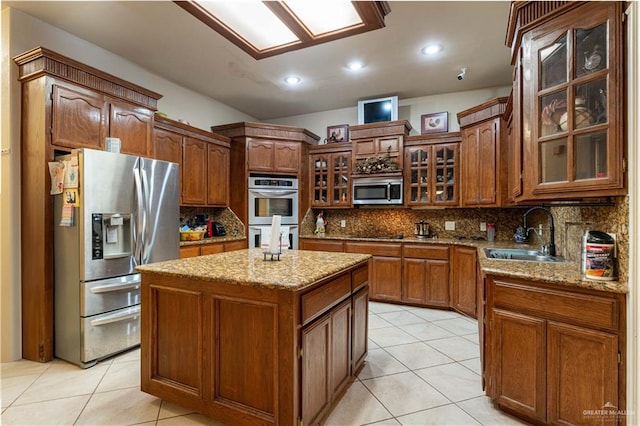 kitchen featuring a center island, sink, stainless steel appliances, light stone counters, and backsplash