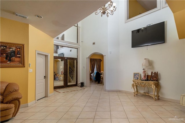 interior space with a towering ceiling, light tile patterned flooring, and an inviting chandelier