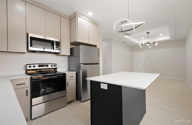 kitchen with stainless steel appliances, hanging light fixtures, light countertops, a center island, and a tray ceiling