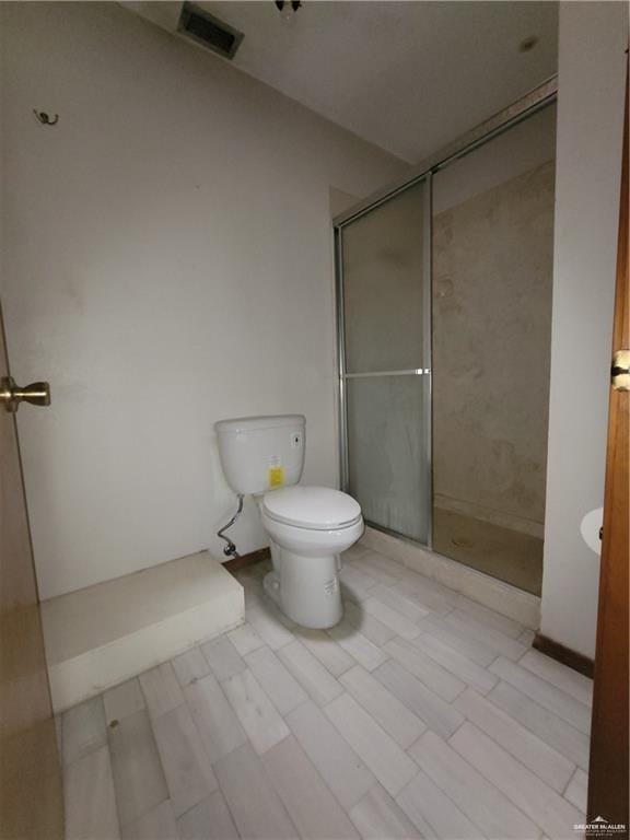 bathroom featuring wood-type flooring, toilet, and a shower with door