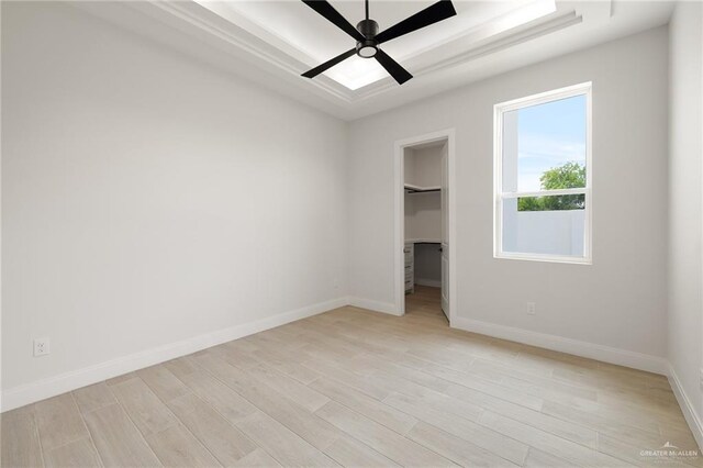 unfurnished bedroom featuring light wood finished floors, baseboards, a spacious closet, and a tray ceiling
