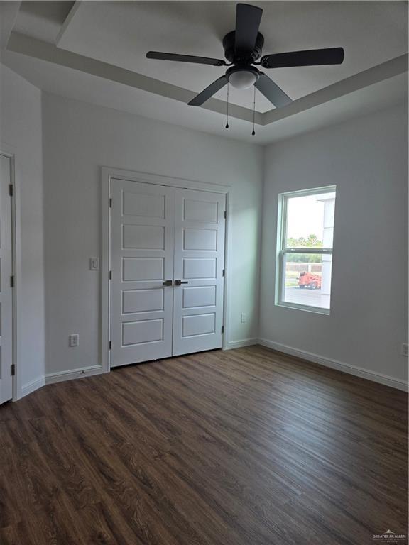 901 E Yuma Ave Unit 206, Mcallen, TX 78503 - unfurnished bedroom with a tray ceiling, a closet, baseboards, ceiling fan, and dark wood-style flooring