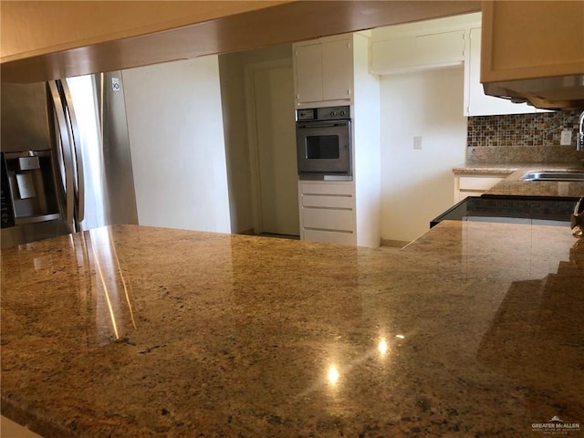 kitchen featuring white cabinets, stainless steel oven, sink, and stone counters