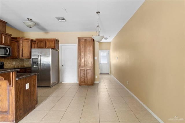 kitchen with backsplash, dark stone counters, stainless steel appliances, light tile patterned floors, and hanging light fixtures