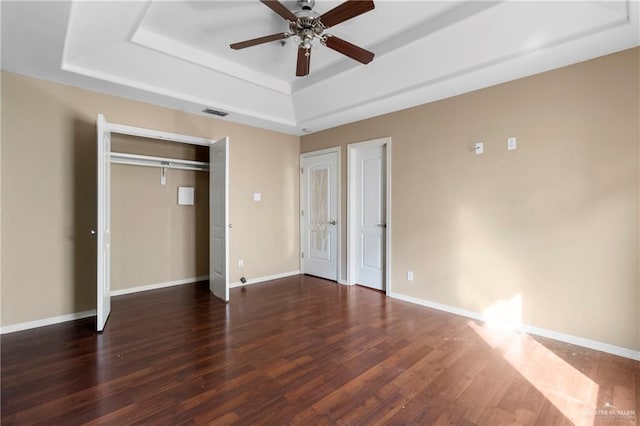 unfurnished bedroom with ceiling fan, dark hardwood / wood-style floors, and a tray ceiling