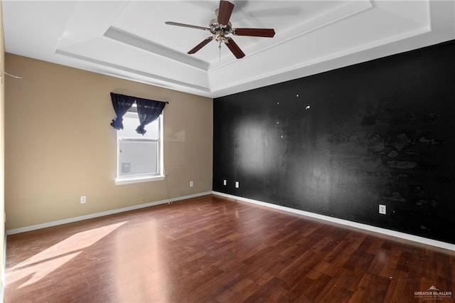 empty room with hardwood / wood-style floors, a tray ceiling, and ceiling fan