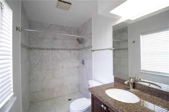 bathroom featuring vanity, a tile shower, and toilet