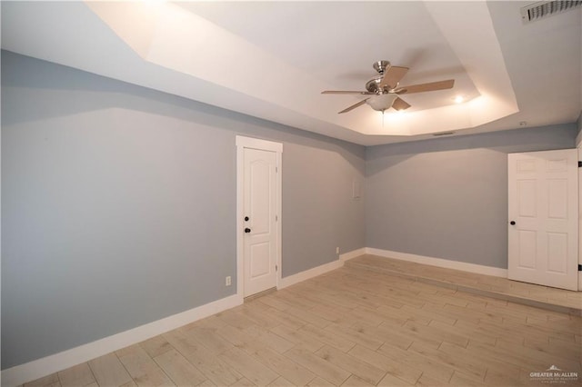 unfurnished room with a ceiling fan, light wood-type flooring, a tray ceiling, baseboards, and visible vents
