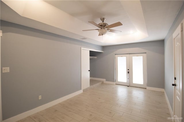 unfurnished room featuring a raised ceiling, french doors, light wood-type flooring, baseboards, and ceiling fan