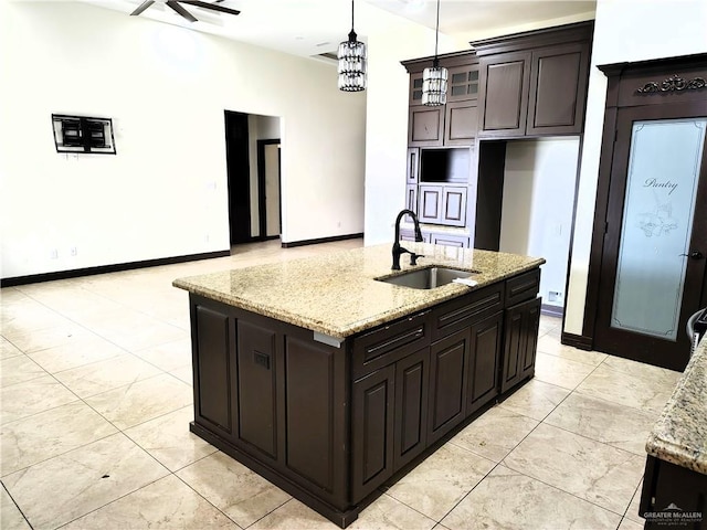 kitchen featuring light stone counters, dark brown cabinets, sink, and a center island with sink